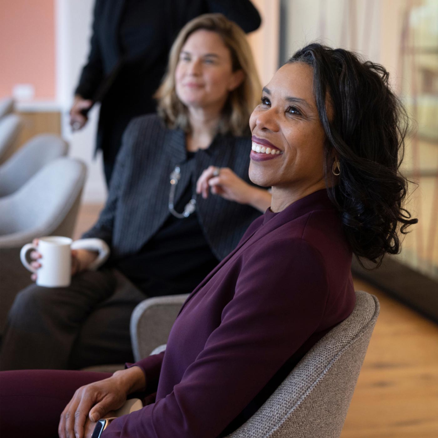 A woman talking to a coworker out of frame in a conference room, with another coworker listening behind her.