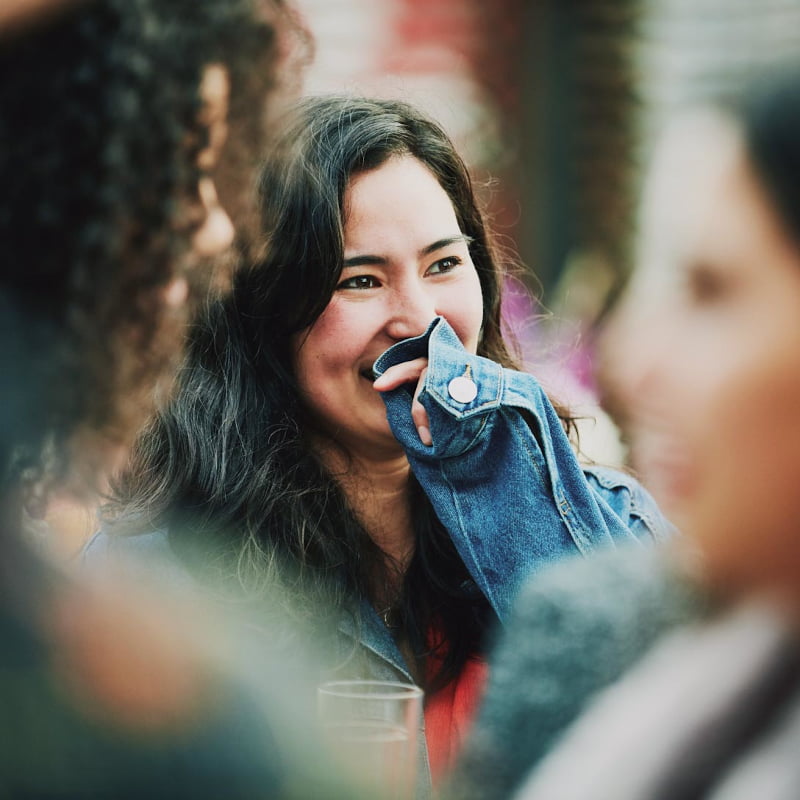 A young girl in a denim jacket holds her hand to her mouth while laughing.