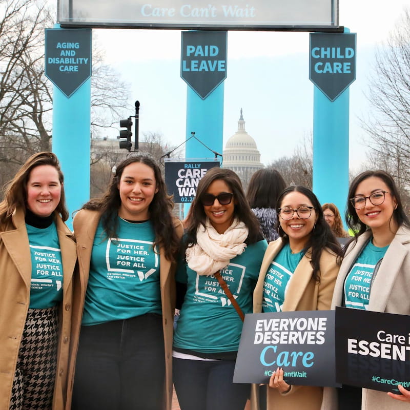 Five women gather at a rally wearing teal shirts that say, "Justice for her. Justice for all." One holds a sign that reads, "Everyone deserves care #CareCantWait."