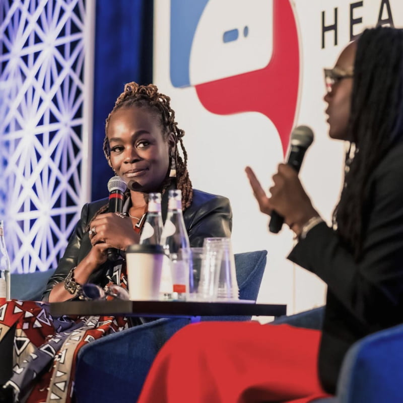 Dr. Alfiee M. Breland-Noble, founder of the AAKOMA Project, sits on a stage with a microphone in hand at a conference.