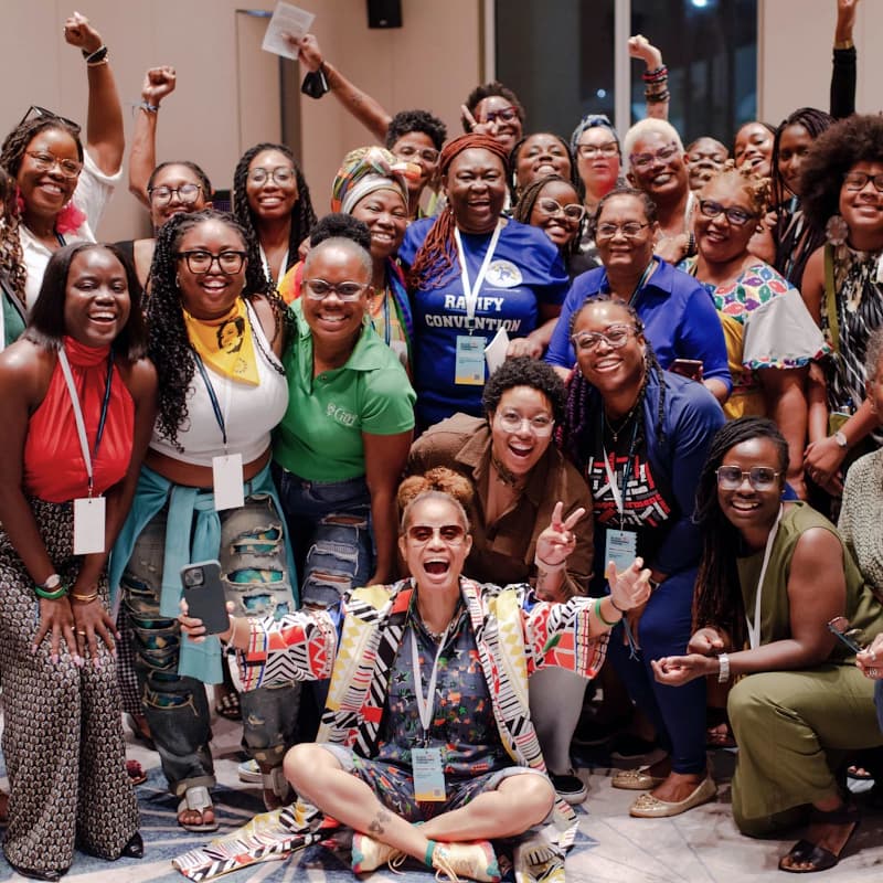 A large group of Black women gather around smiling and posing for the camera.