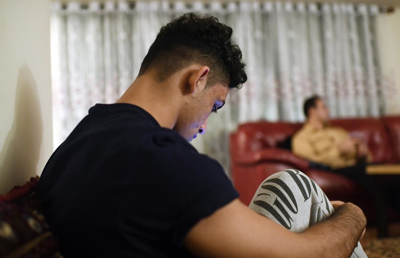 A young man looks down at his phone while sitting on a living room couch.