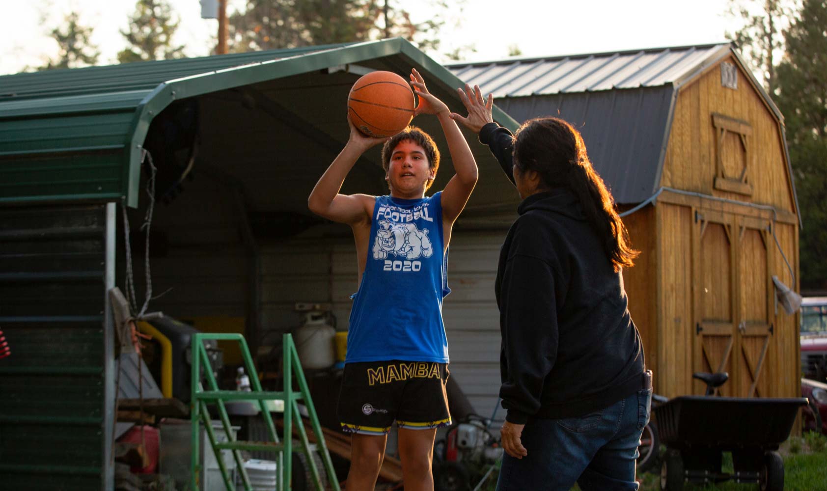 A 13-year-old boy shoots a basketball while his 62-year-old grandaunt looks on.