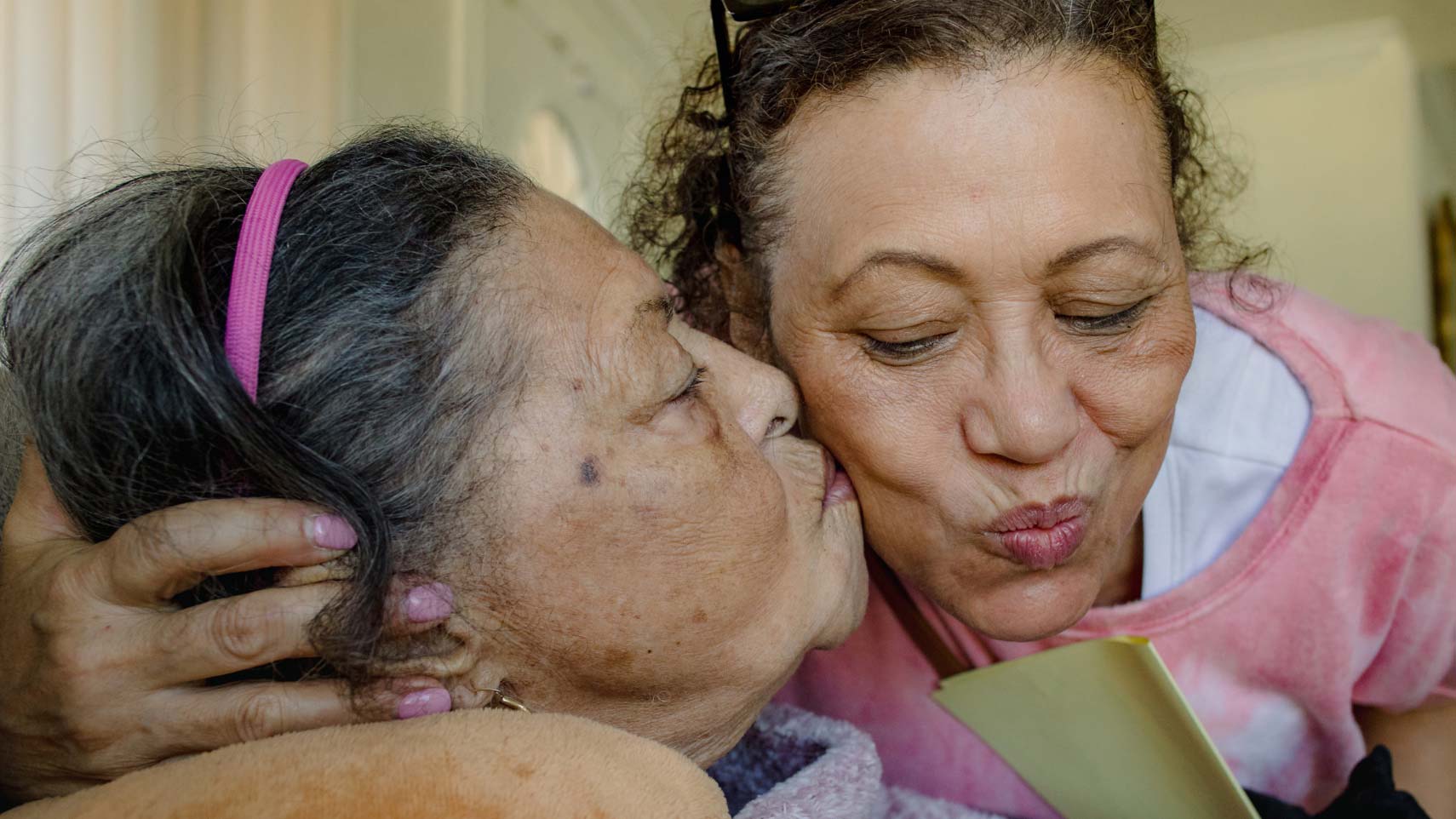 An aging woman kisses her daughter's cheek.