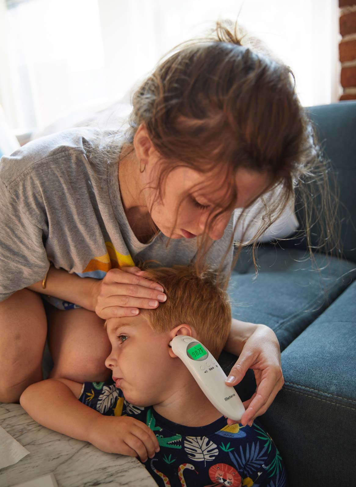 A 32-year-old woman holds a thermometer up to her 4-year-old son's ear.