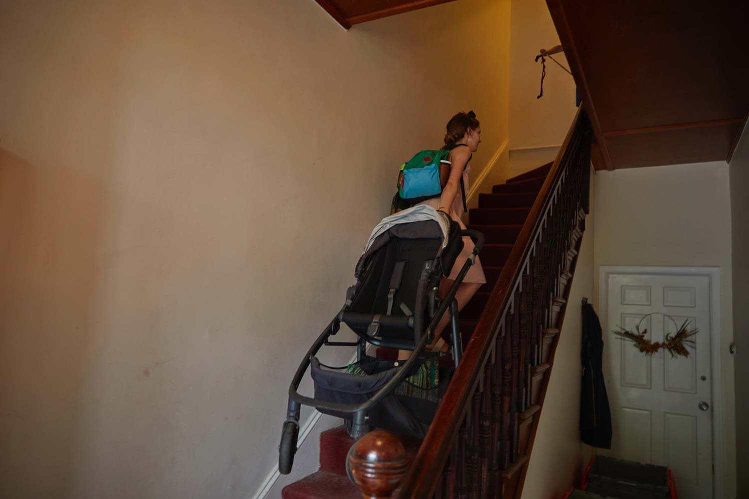 A 32-year-old woman drags a stroller up a flight of stairs while carrying a bag.