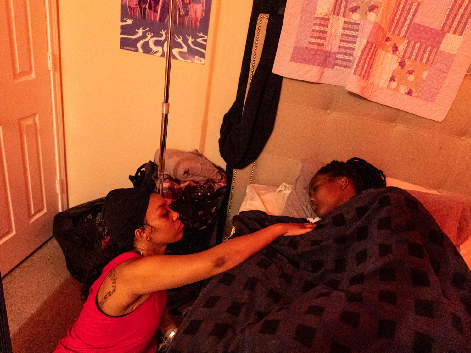 A 40-year-old woman reaches out to touch her 16-year-old daughter, who lies in bed under a blanket.