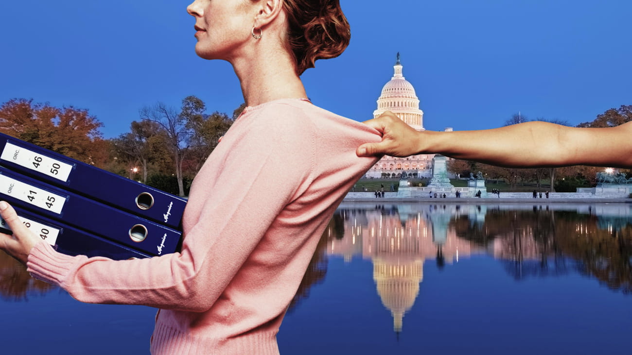 A hand holds the back of a shirt of a woman's shirt, preventing her from continuing forward.