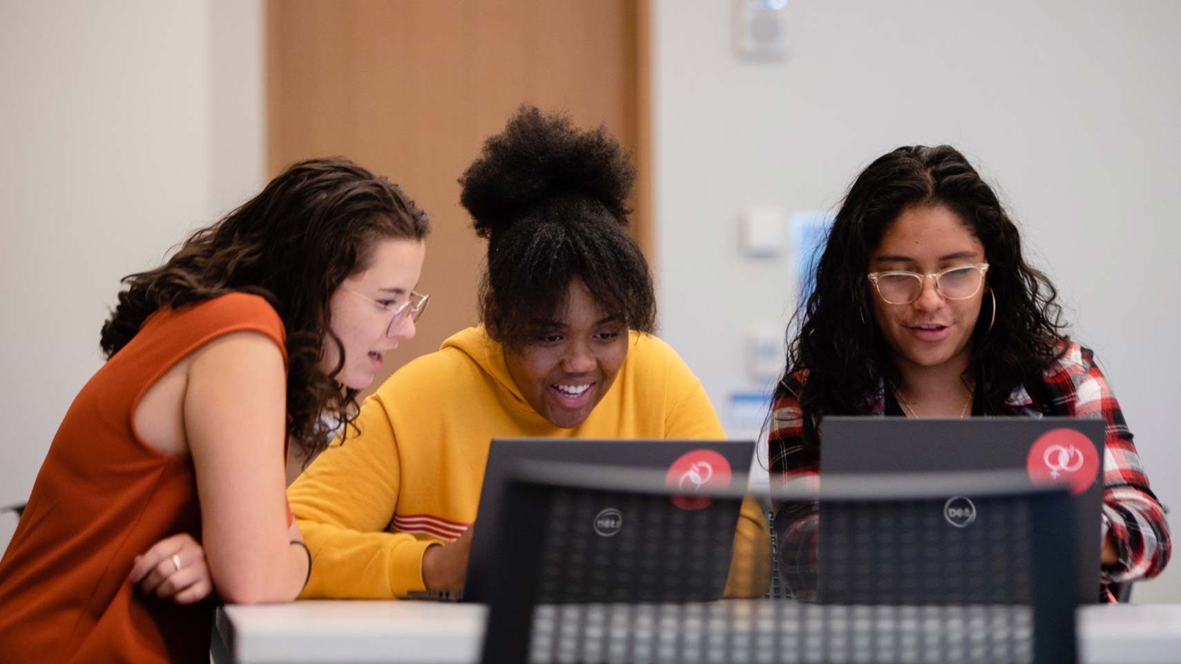 Three students sit smiling and looking at computers.