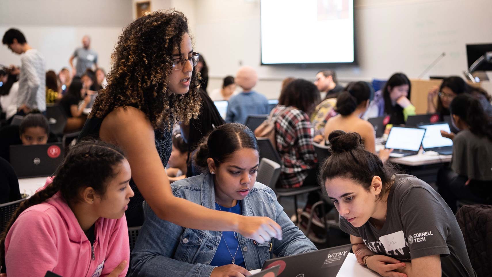 A person points at a laptop computer while a small group of other people look at the screen.