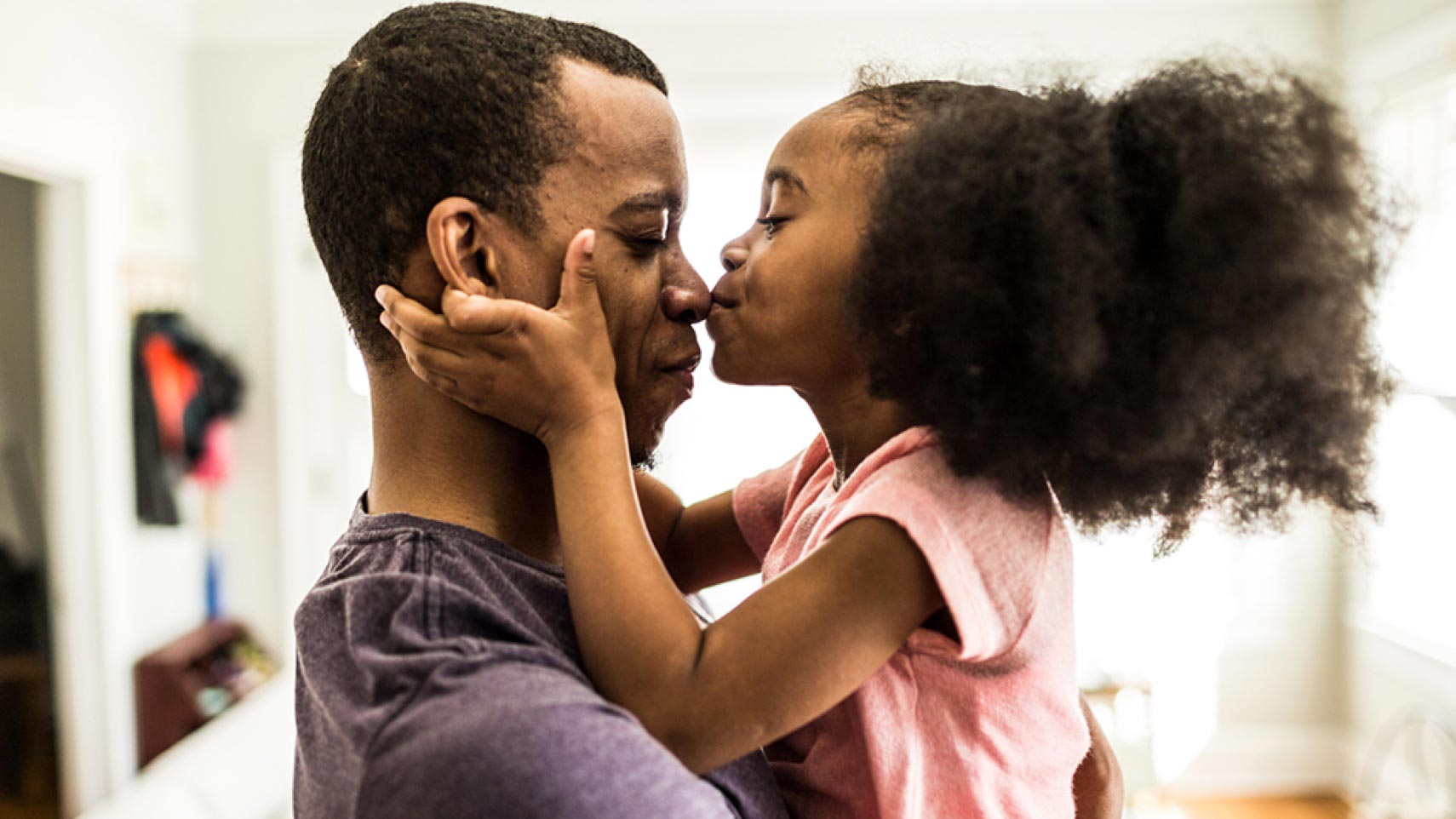 A child holds a person's face in her hands and kisses their nose.