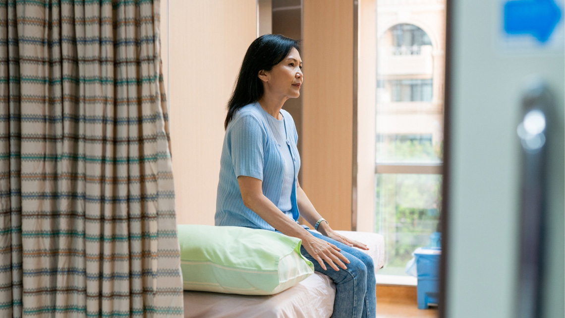 A woman sits on an exam bed in a hospital exam room.