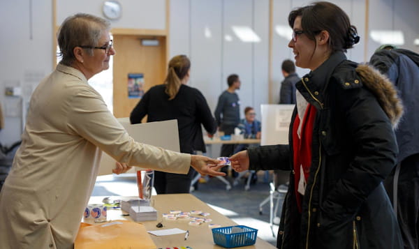 A woman hands an "I voted" sticker to a voter at a polling place.