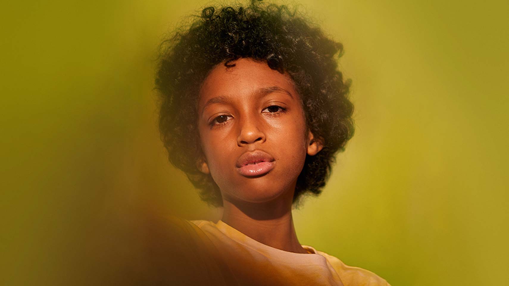 A close-up of a child's face in front of an out-of-focus yellow background.