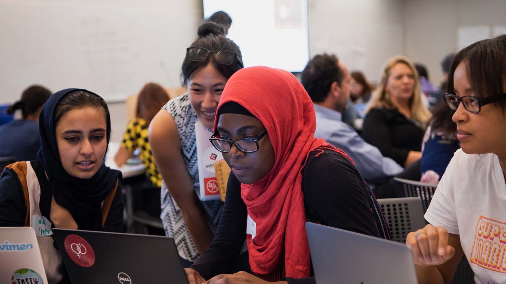 Students gather around a laptop computer.