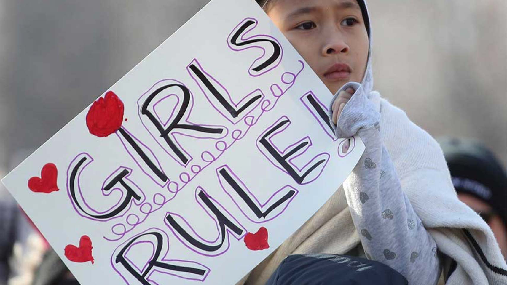 A child holds a handmade sign that reads, "GIRLS RULE!"