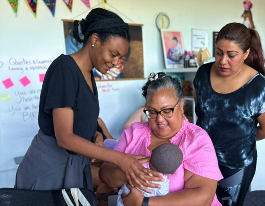 A woman smiling while holding her baby as a care worker speaks to them.