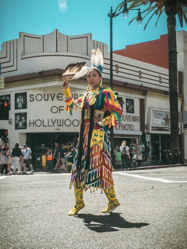 A brightly dressed Indigenous woman stands on the street outside a busy souvenir store.