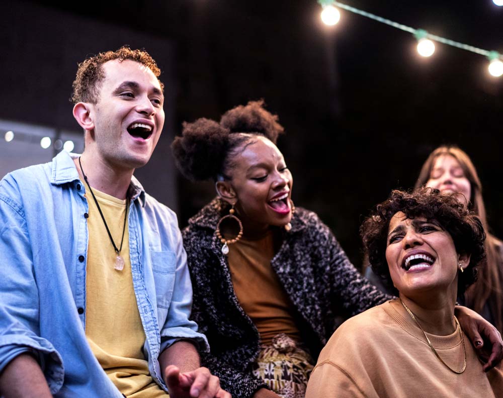 Four young friends hanging out on a patio at night, singing along to the same song.
