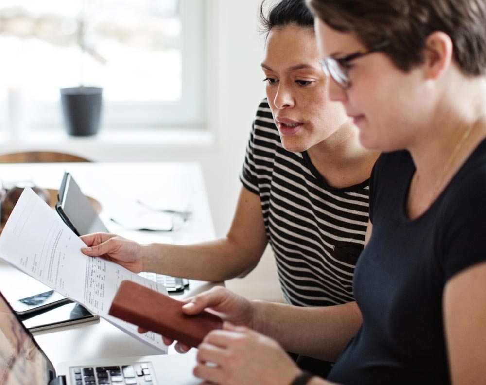 Two women discussing their finances and working together at their dining table.