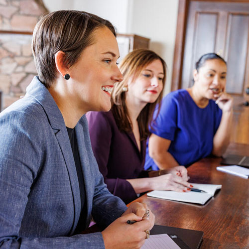 Three women participating in a meeting at a conference table in a professional office setting.
