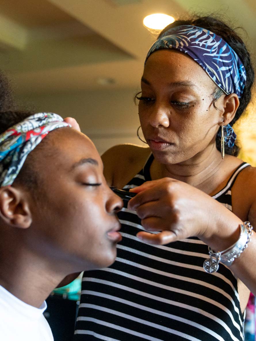 A mother applies makeup to her teenager daughter's face.