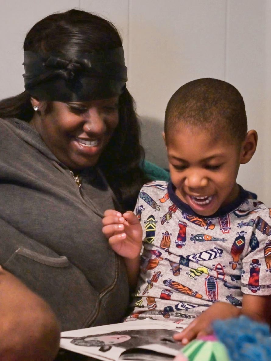 An mother and a son smile as they look at a picture book together.