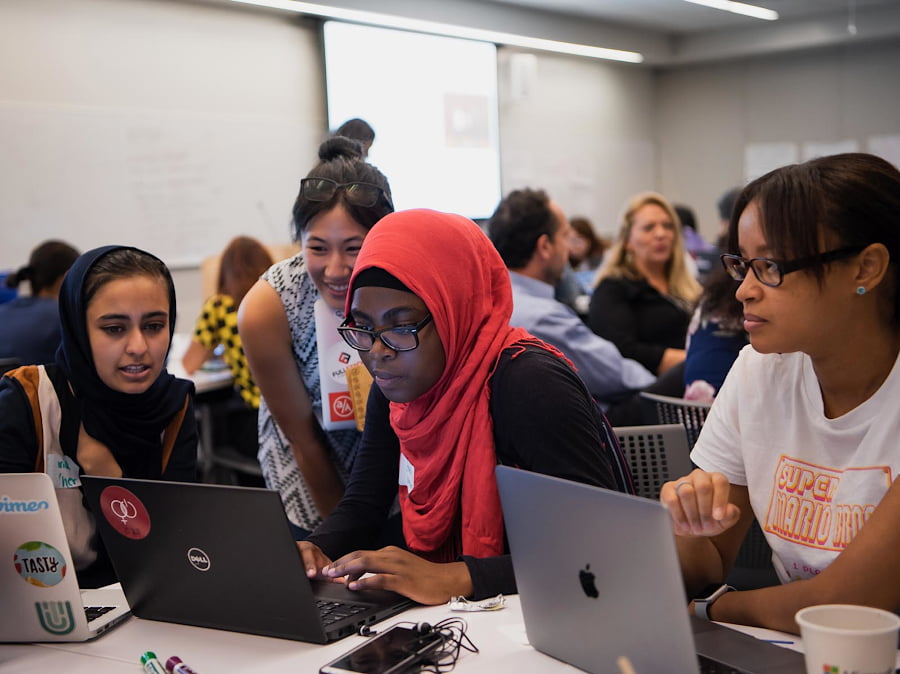 Students gather around a laptop computer.