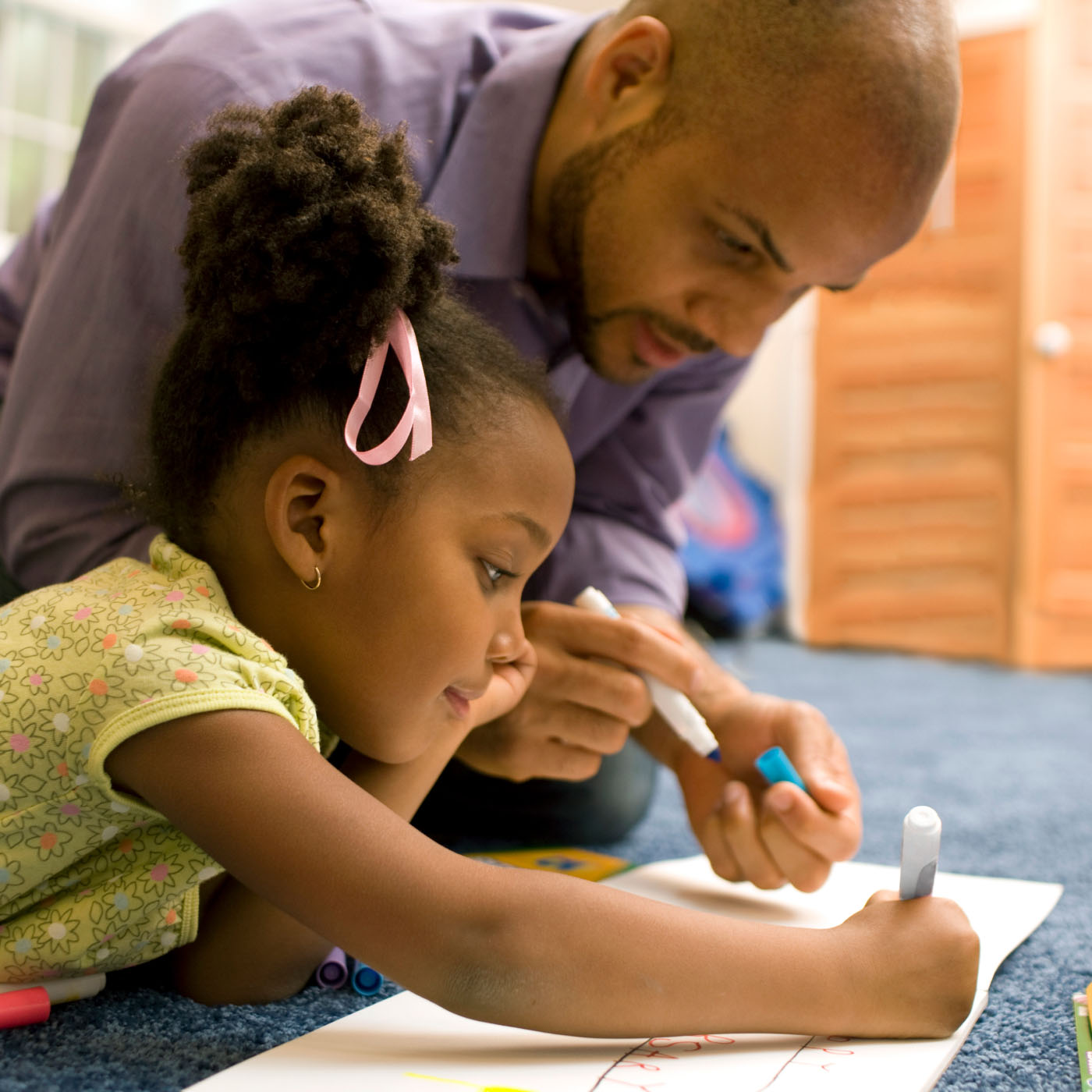 A father helping his daughter color in a book on the floor