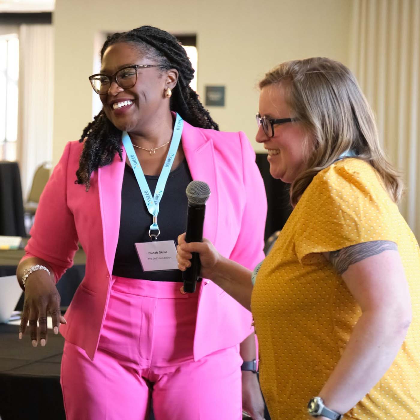 Two women interact with the audience at a conference on student mental health.   
