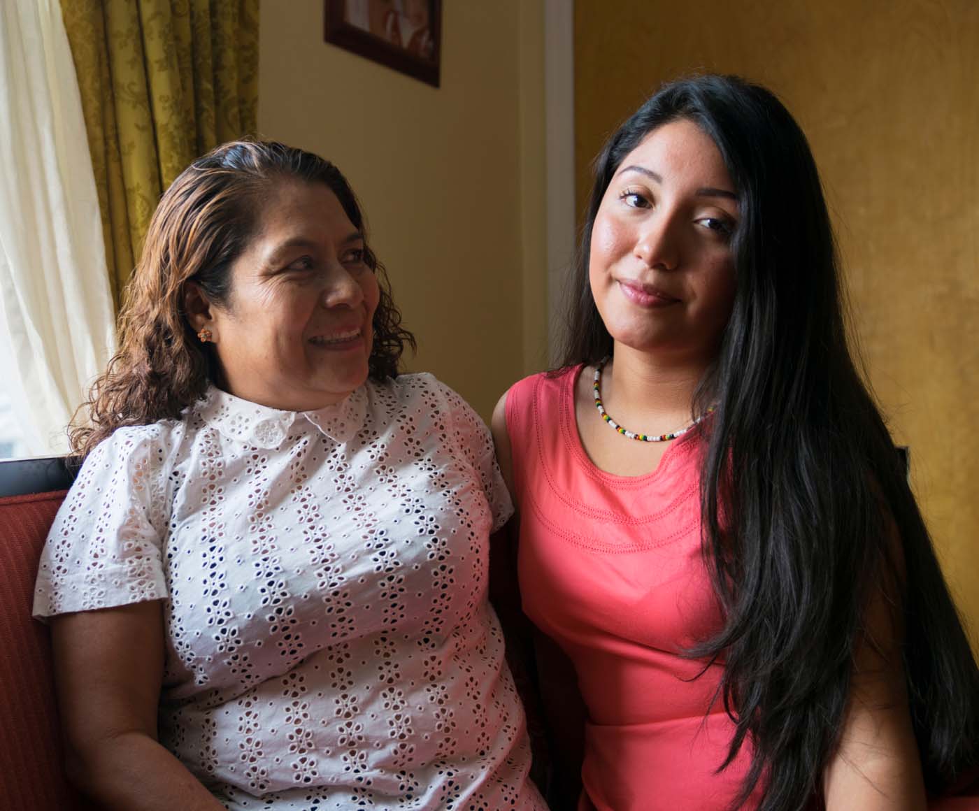 A young woman sits on a couch with her arm around her mother