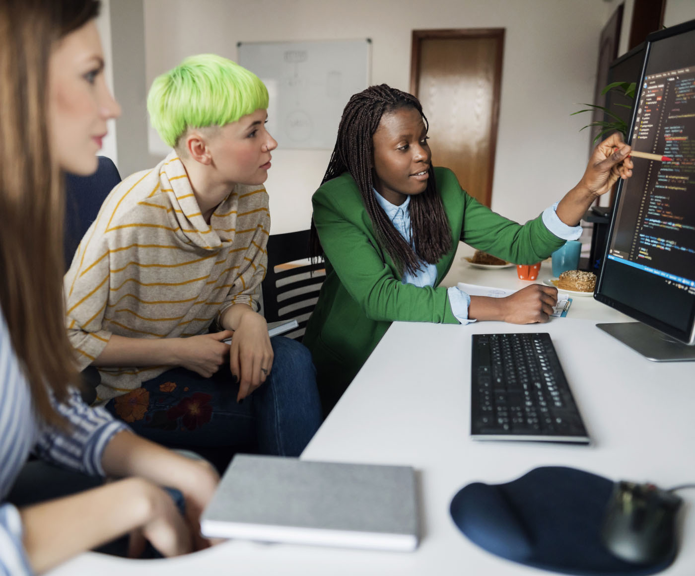 Three young female computer programmers looking at a monitor and working together in an office.