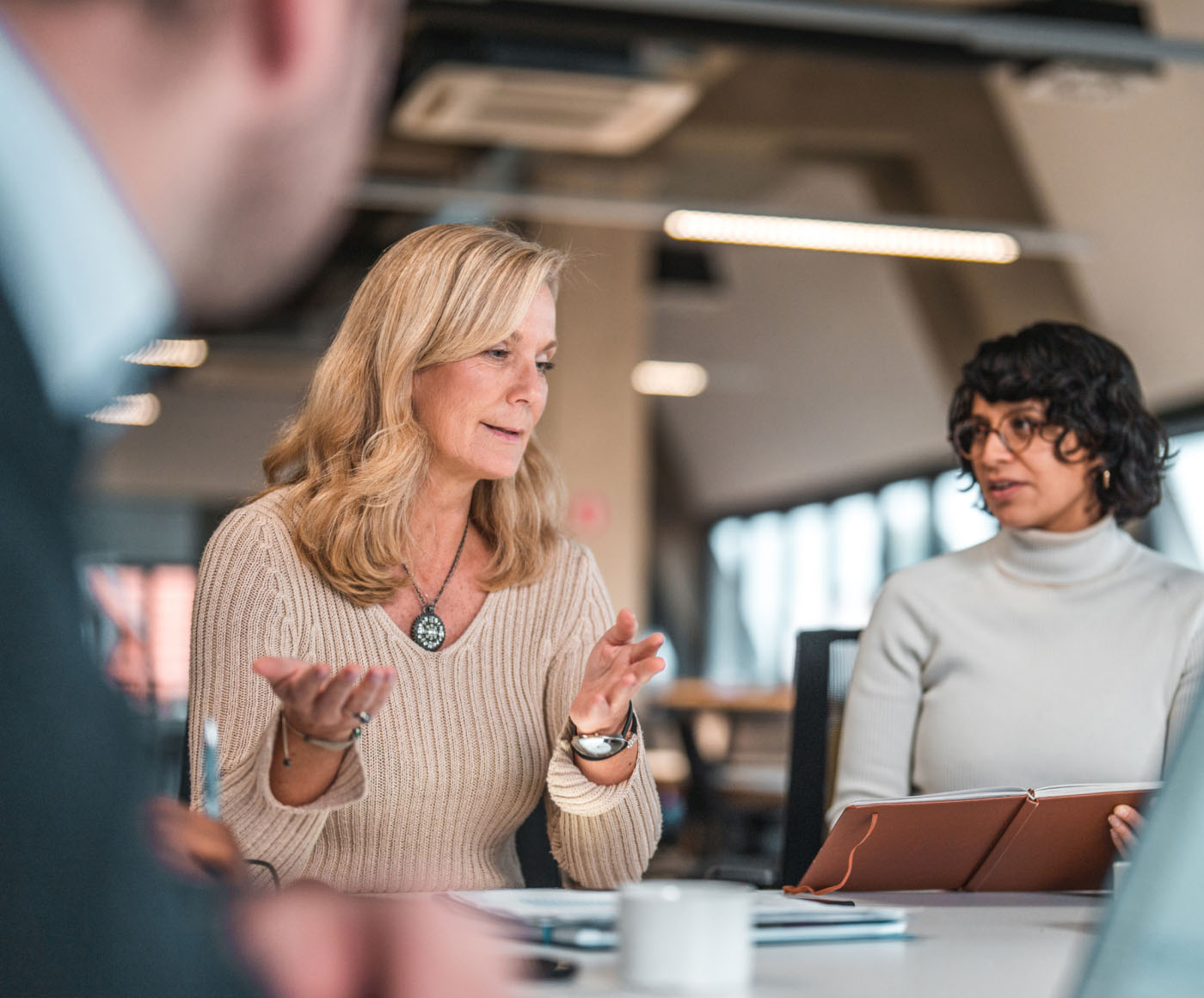 A woman having a conversation with a group of her colleagues at a table in their office.