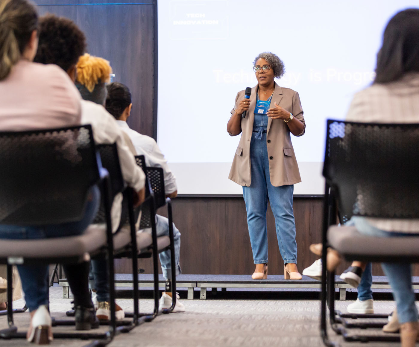 A woman speaking into a microphone and delivering a presentation to an audience