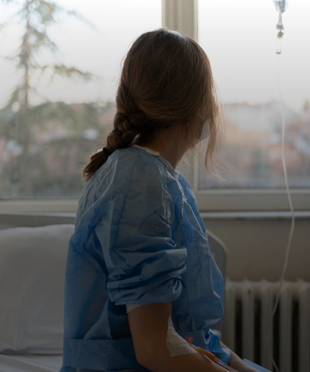 A woman in a hospital gown looks out the window of her exam room.