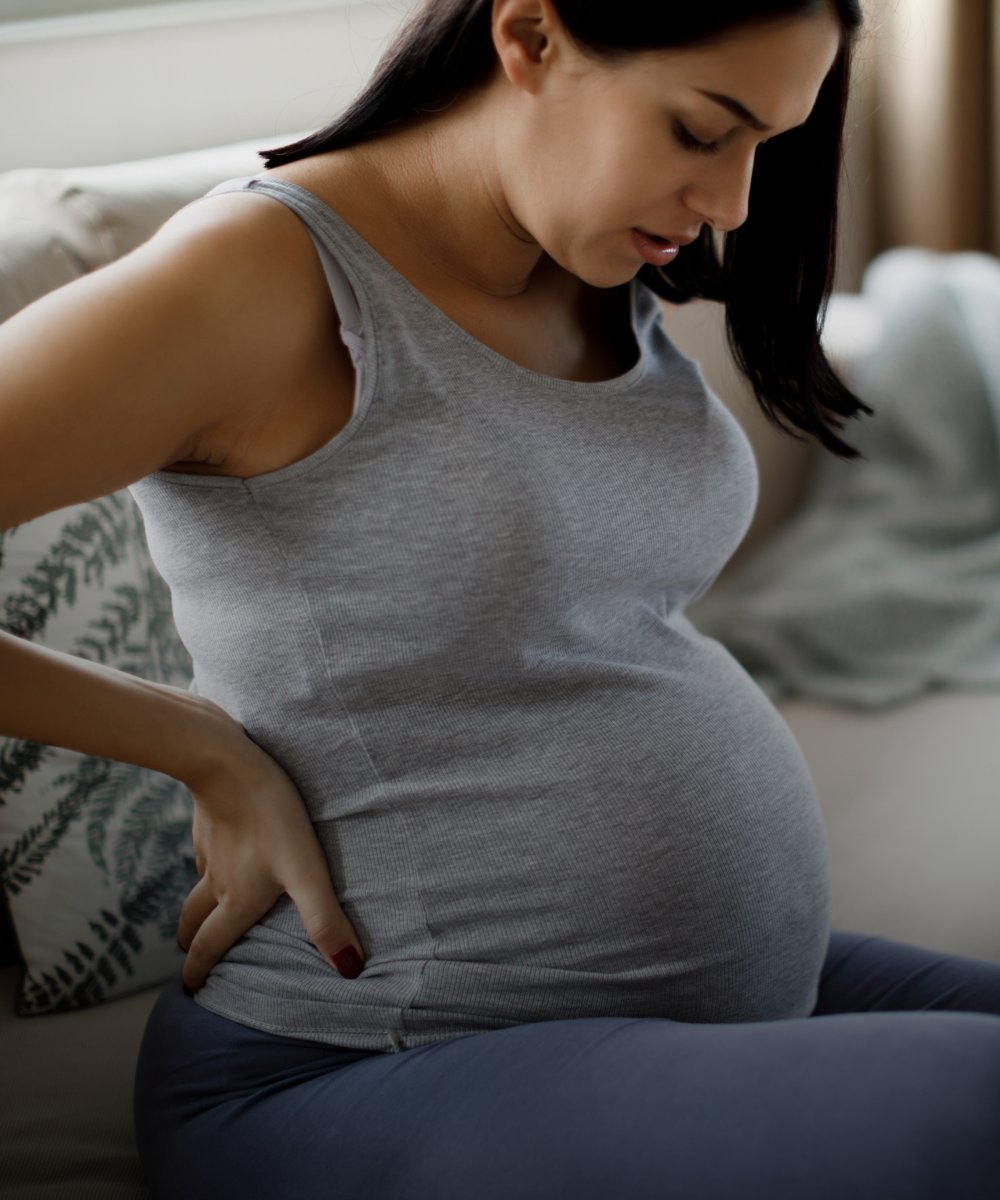 A pregnant woman sitting on a couch, trying to deal with lower back pain.