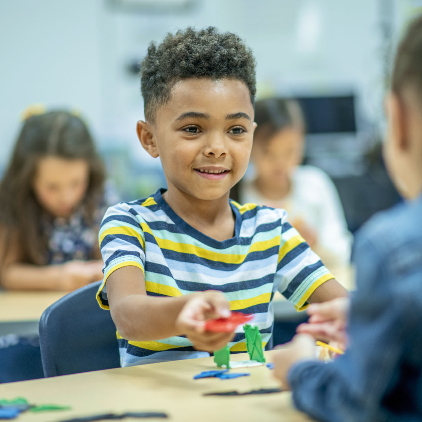 A young student sharing blocks with his classmate across the table