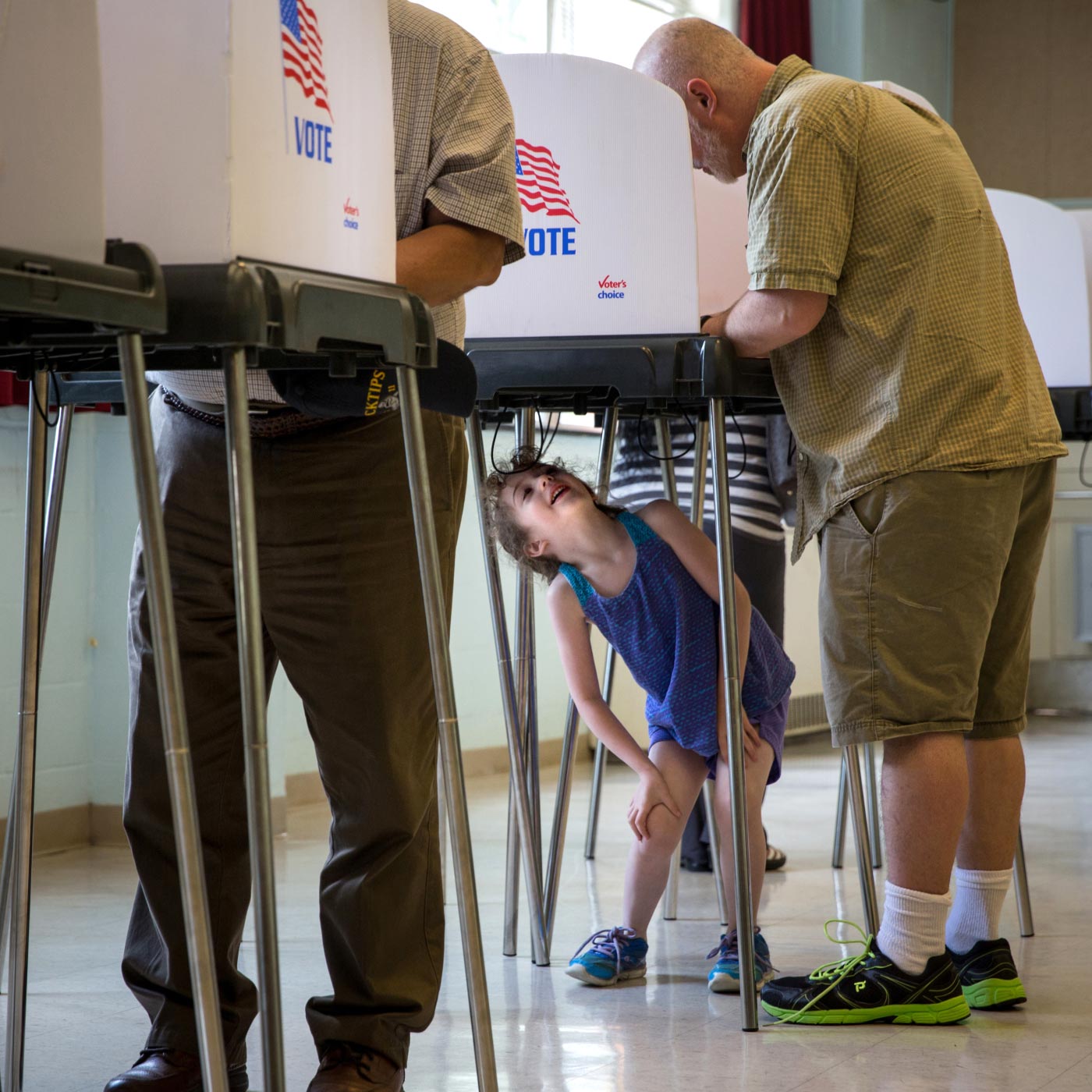 A young girl plays under a voting booth while her older relative votes in a primary election.