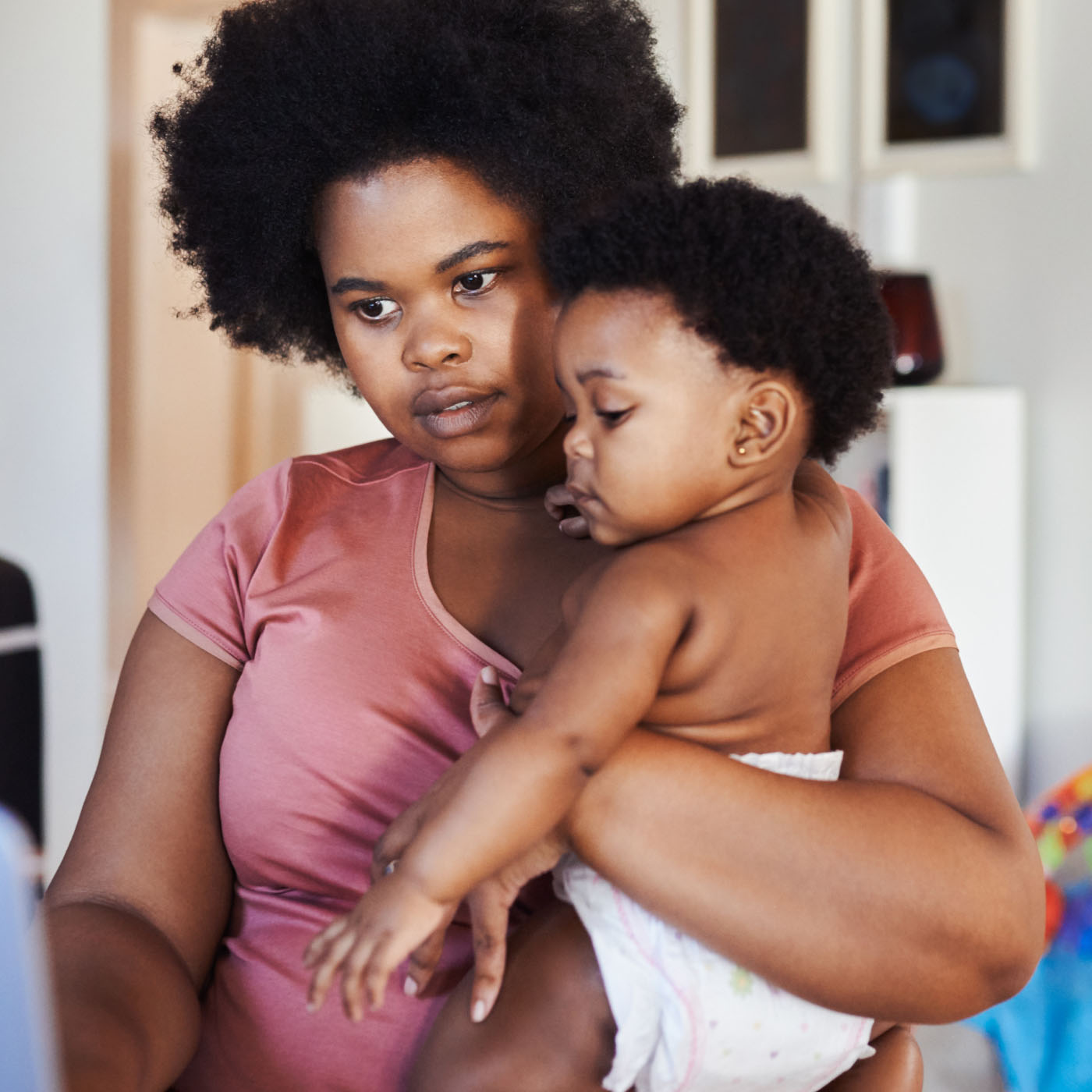A mother holding her baby on her hip with one hand and typing on a laptop with the other hand