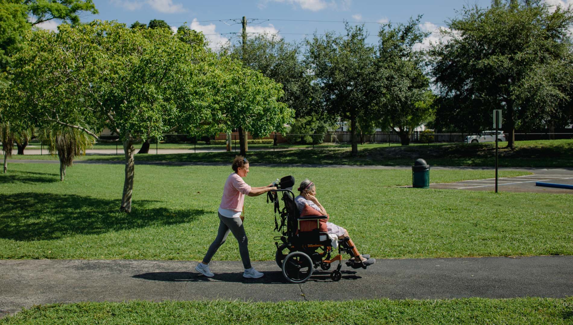 A woman pushes her mother's wheelchair during their weekly trip to a local park, as her mother's caregiver
