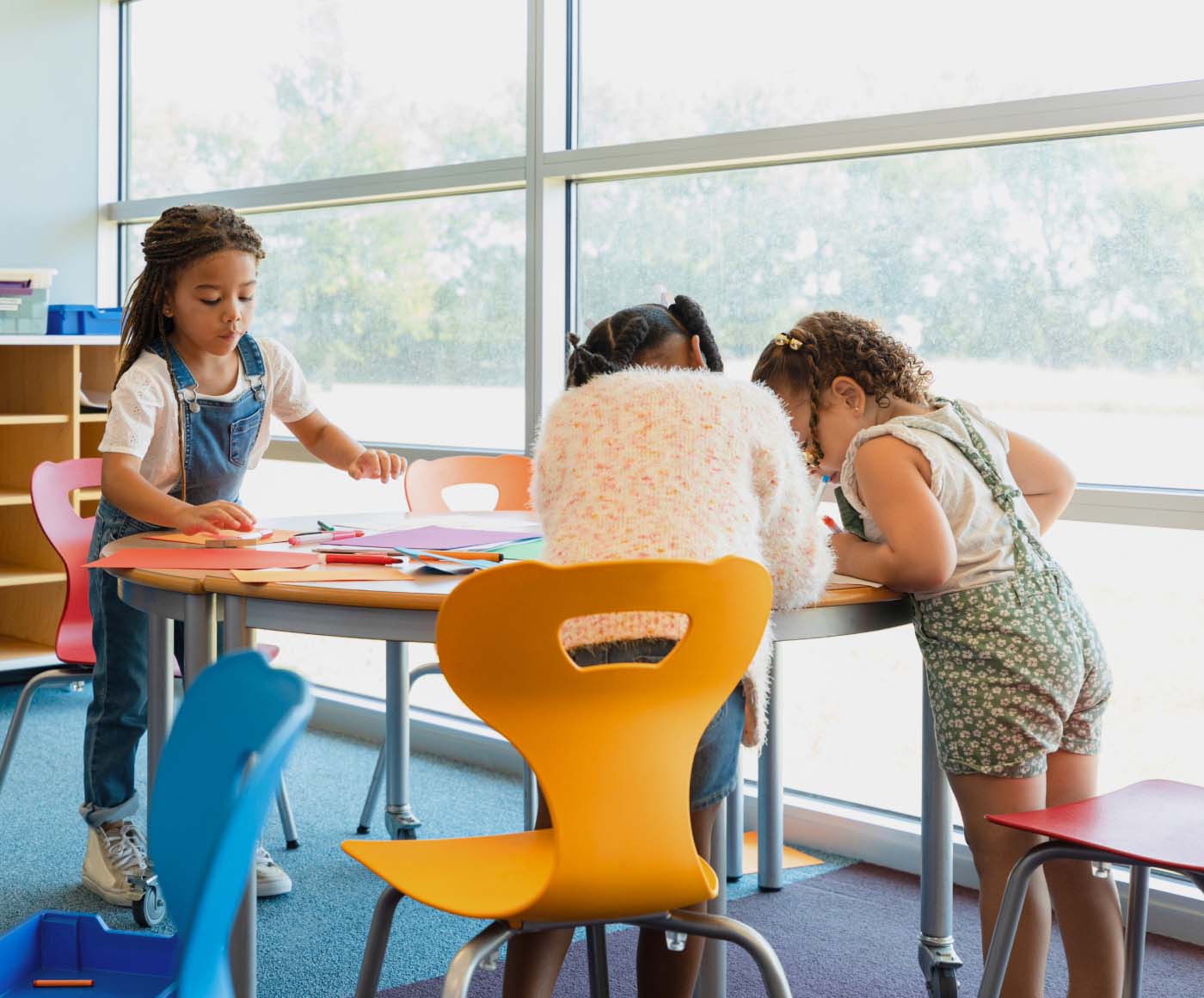 Three young children work together on a craft at a school table