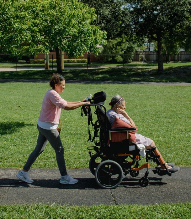 A woman pushes her mother's wheelchair during their weekly trip to a local park, as her mother's caregiver.
