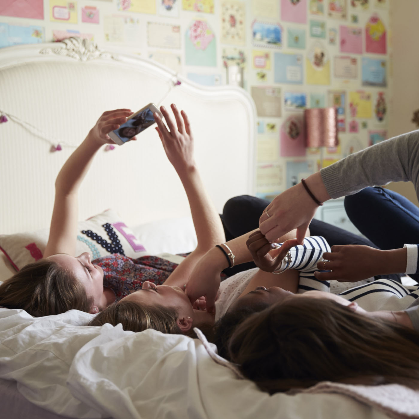 Three girls lying on a bed side-by-side taking a selfie together