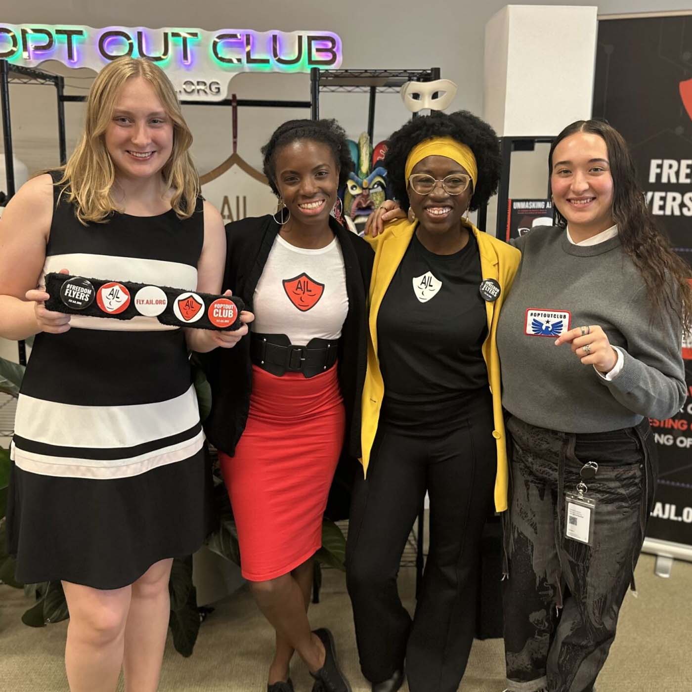 Four women holding and wearing AJI merchandise smiling for a photo at a summit event