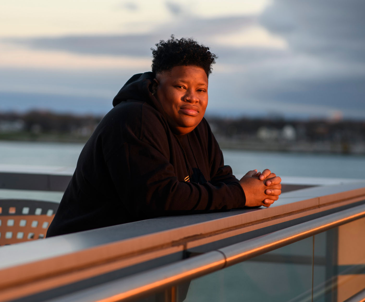 A person standing on a balcony and looking toward the camera during sunset