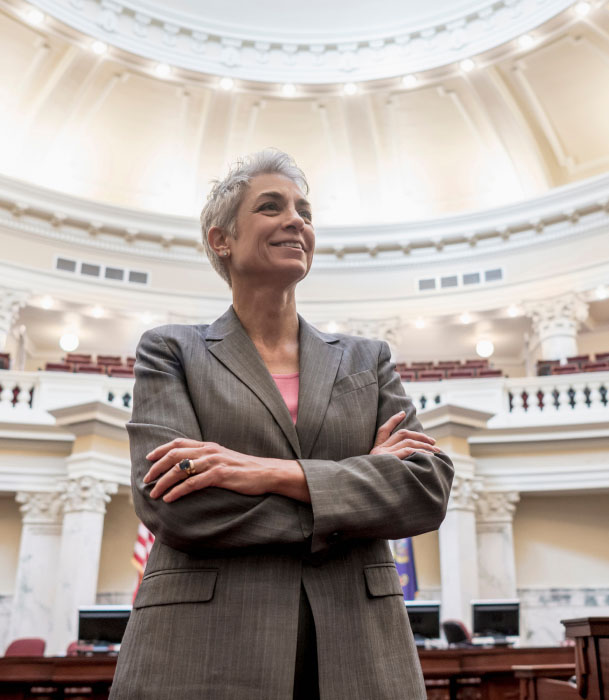 A female politician stands in a capitol building with her arms crossed.